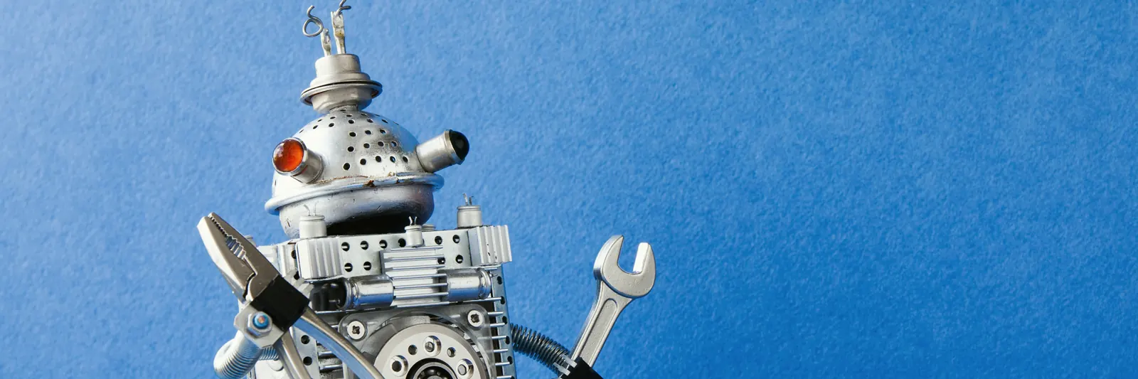Metalowy robot z kluczem płaskim i szczypcami na niebieskim tle — automatyzacja bez ręcznej pracy