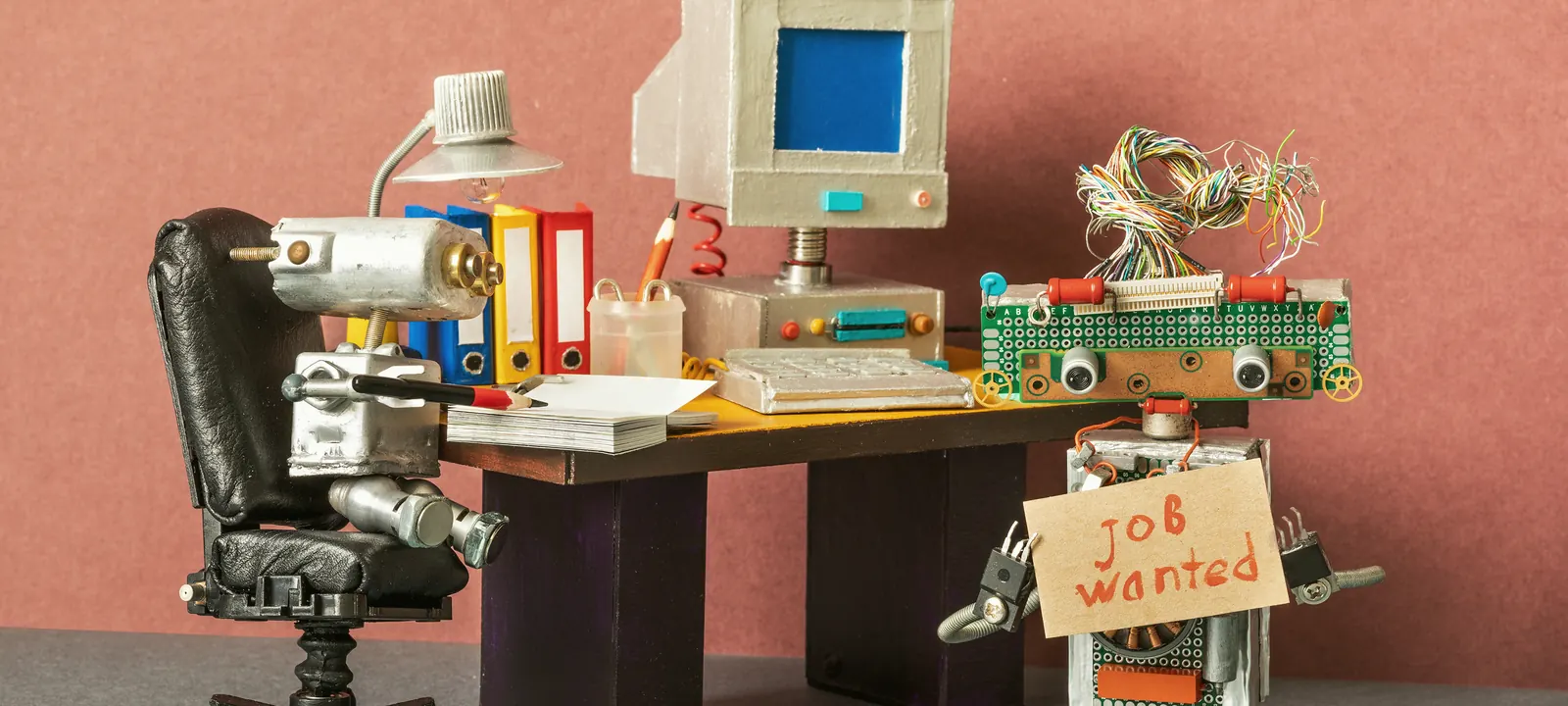 Rozmowa kwalifikacyjna robotów — rekruter za biurkiem i kandydat z tabliczką job wanted